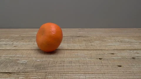 Mandarin rolls and stops in the middle of a wooden surface on a gray background. 動画素材 266985729