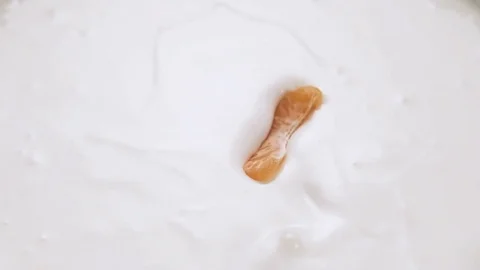 Mandarin slices falling into yogurt with splashes, slow motion. Stock Footage 84953433