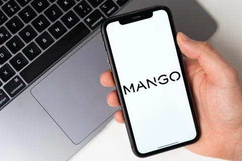 Mango app on the screen of smartphone in mans hand with a laptop on the Stock Photos