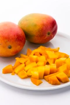 Mango cubes and two whole mangos on a white plate Stock Photos