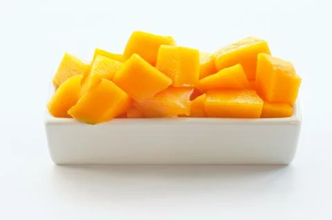 Mango cut in cubes on a white dish against white background Stock Photos
