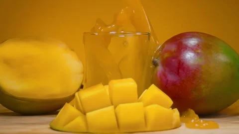 Mango Juice Poured Into Glass Next to Diamond Cut Mango on Yellow Stock Footage 334337491