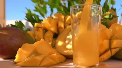 Mango Juice Poured Into Glass Next to Ripe Mango Pieces on Skin Stock Footage 334337530