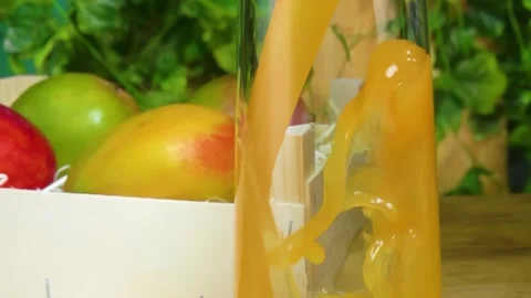 Mango Juice Poured Into Glass Next to Mango in Crate Stock Footage 336078507