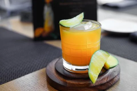 Mango juice on restaurant table with raw mango slice on side Stock Photos