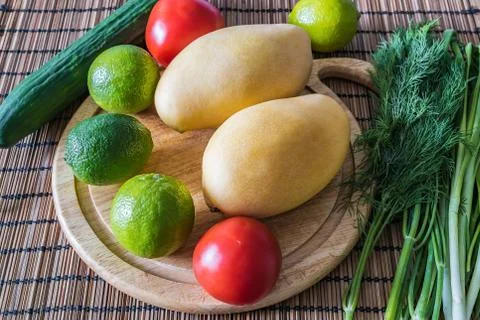 Mango, lime, tomatoes, cucumber and greens on the kitchen table Stock Photos