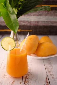 Mango mocktail and plate of mango. Vase with tropical leaves on left Stock Photos