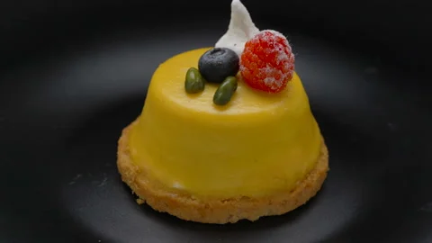 Mango mousse cake covered with yellow glaze rotating on black plate Stock Footage 99251778