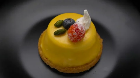 Mango mousse cake dessert covered with yellow glaze rotating on black plate Stock Footage 99251652