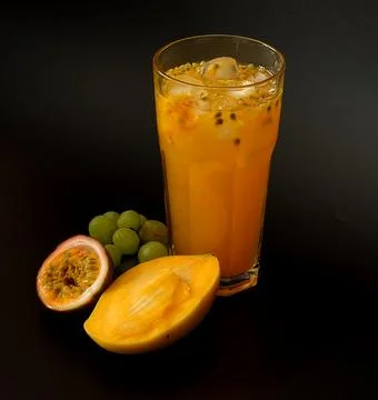 Mango, passion fruit and grape juice with ice in a tall faceted glass on a .. Stock Photos