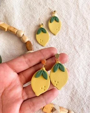 Mango shape yellow color earring on female hand. Modern jewelry earring for.. Stock Photos