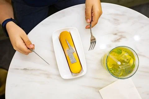 Mango yellow eclair with silver decor on top. Lemonade in a glass. Hands and Stock Photos