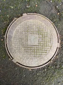 A manhole cover on the ground with a grid pattern on it Stock Photos