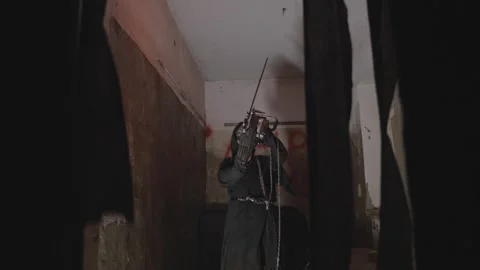 Maniac in the clothes of an executioner holds a chainsaw in his hands. Abandoned Stock Footage 240274340