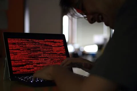 Maniac hacker laughing at red binary screen. computer crime data stealing and Stock Photos