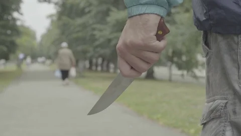 A maniac with a knife follows an elderly woman in a park. The murderer. Killer Stock Footage