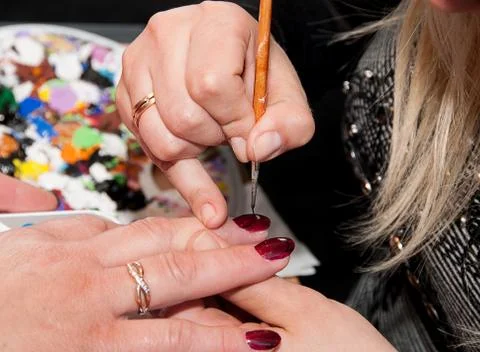 Manicure. Applying a thin brush pattern on the dark red base Stock Photos