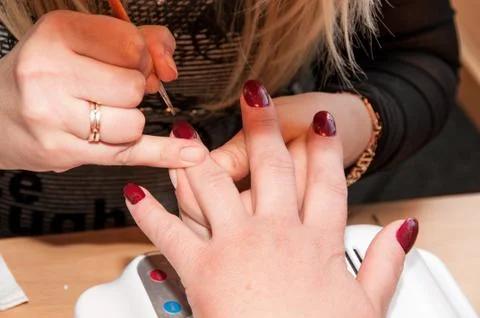 Manicure. Applying a thin brush pattern on the dark red base Stock Photos