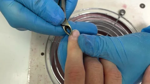 A manicure master in blue gloves uses a metal tool to process the cuticle on her Stock Footage 165529742