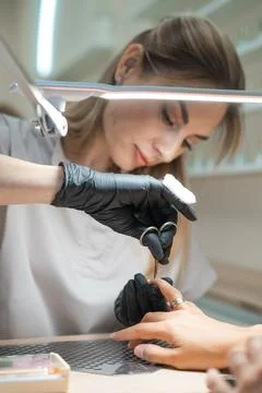 Manicure master cutting nails by scissors on a womans hand in black gloves Stock Photos