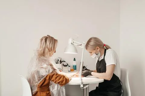 Manicure master makes nails cute pretty young woman in beauty salon. Customer Stock Photos