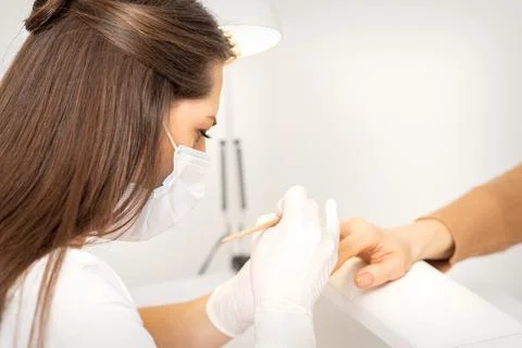Manicure master in protective face mask and white gloves apply polish to female Stock Photos