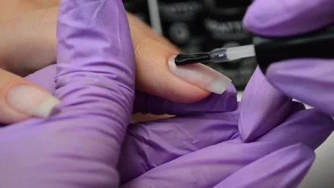 Manicure master in purple gloves apply transparent nail Polish on the client's Stock Footage 132021817