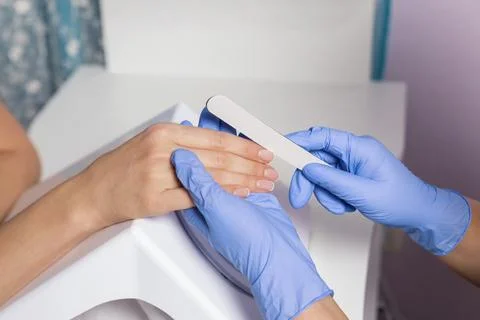 Manicure process. A master in blue gloves polishes a client's nails. Stock Photos