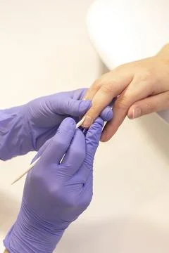 Manicure technician pushes back client cuticles, holding wooden cuticle remover Stock Photos