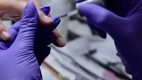 A manicurist applying a protective base coat to the woman's nails Stock Footage 258330077