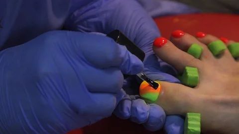 A manicurist gently puts a colored drawing on the toenails of a woman. doing man Stock Footage 119227135