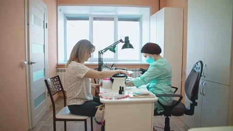 A manicurist paints nails for a client, drying nails in ultra violet. Stock Footage 152987413