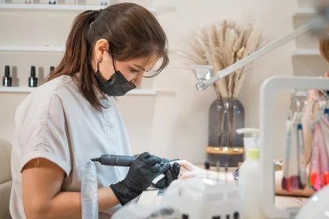 A manicurist sharpens nails with a drill machine during the procedure Stock Photos