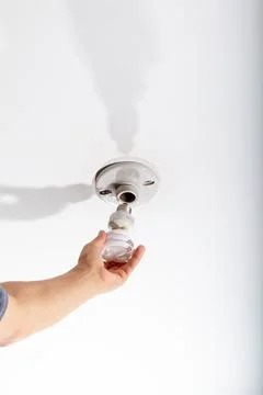 Mano replacing an energy saving light bulb in the ceiling of his room. Stock Photos