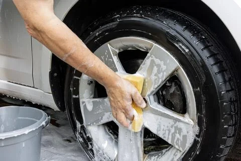 Man's arm with soapy yellow sponge cleaning alloy wheel Stock Photos