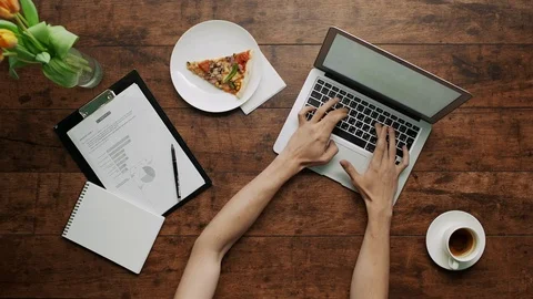 Man's arms typing on laptop checking papers writing Wooden table pizza slice 스톡 동영상 69912282