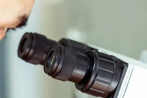 The man's eye is looking through the microscope. Black eyepieces of professional Stock Photos