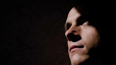 A man's face moves smoothly out of the shadows and into the light Stock Footage 151554531