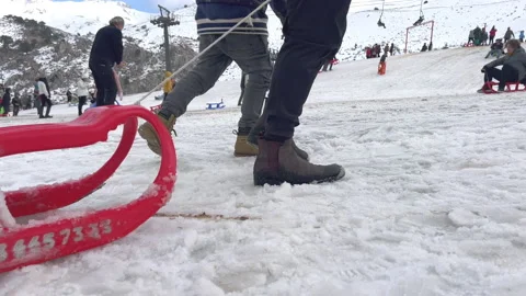 Mans feet walking on snow pulling plastic red sleigh behind them Stock Footage 231699528