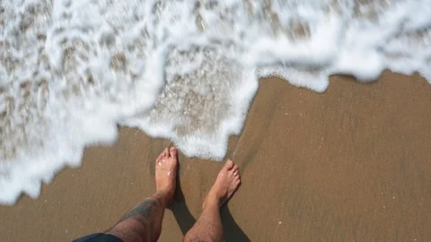 Man's feet washed by ocean waves and buries them in the sand. Point of view of Stock Footage 86233137