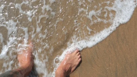 Man's feet washed by ocean waves and buries them in the sand. Point of view of Stock Footage 86235085