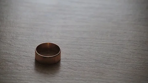 Man's gold wedding ring rolling to woman's one on a table Stock Footage 97955074