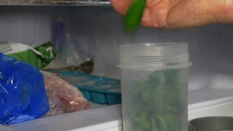 A man's hand adding fresh chilli peppers to a freezer container. Stock Footage 252125846