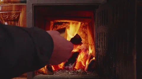Man's Hand Adding Wood to Fire in Traditional Terracotta Stove Stock Footage 327975996