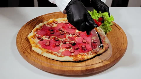 A man's hand in black gloves cuts a delicious, juicy pizza that lies on a wooden Stock Footage 252290579