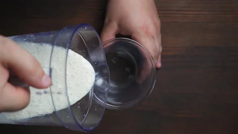 Mans hand with blender cup in hand pouring banana milk shake in to a disposable Stock Footage 133629474