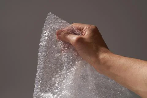 A man's hand bursts bubbles from the bubble wrap. Stock Photos