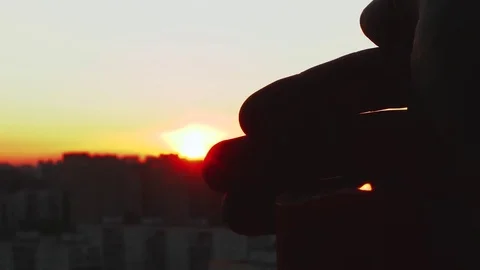 Man's hand closes the flame of the candle from the wind at sunset against the Video stock 76154215