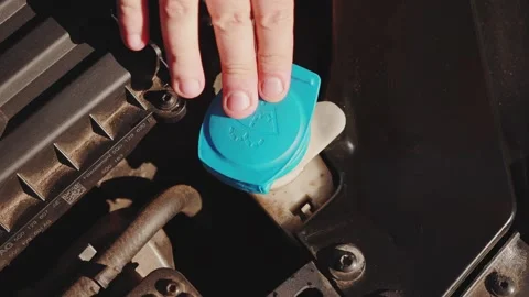 A mans hand closes the lid of the windshield wiper reservoir after filling with Stock Footage 256874539