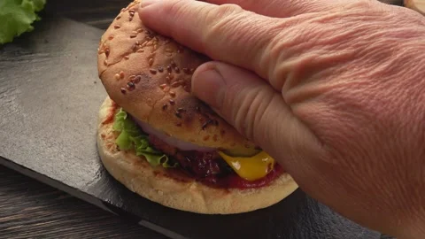A man's hand covers a assembled hamburger with a toasted bun Video stock 233614736